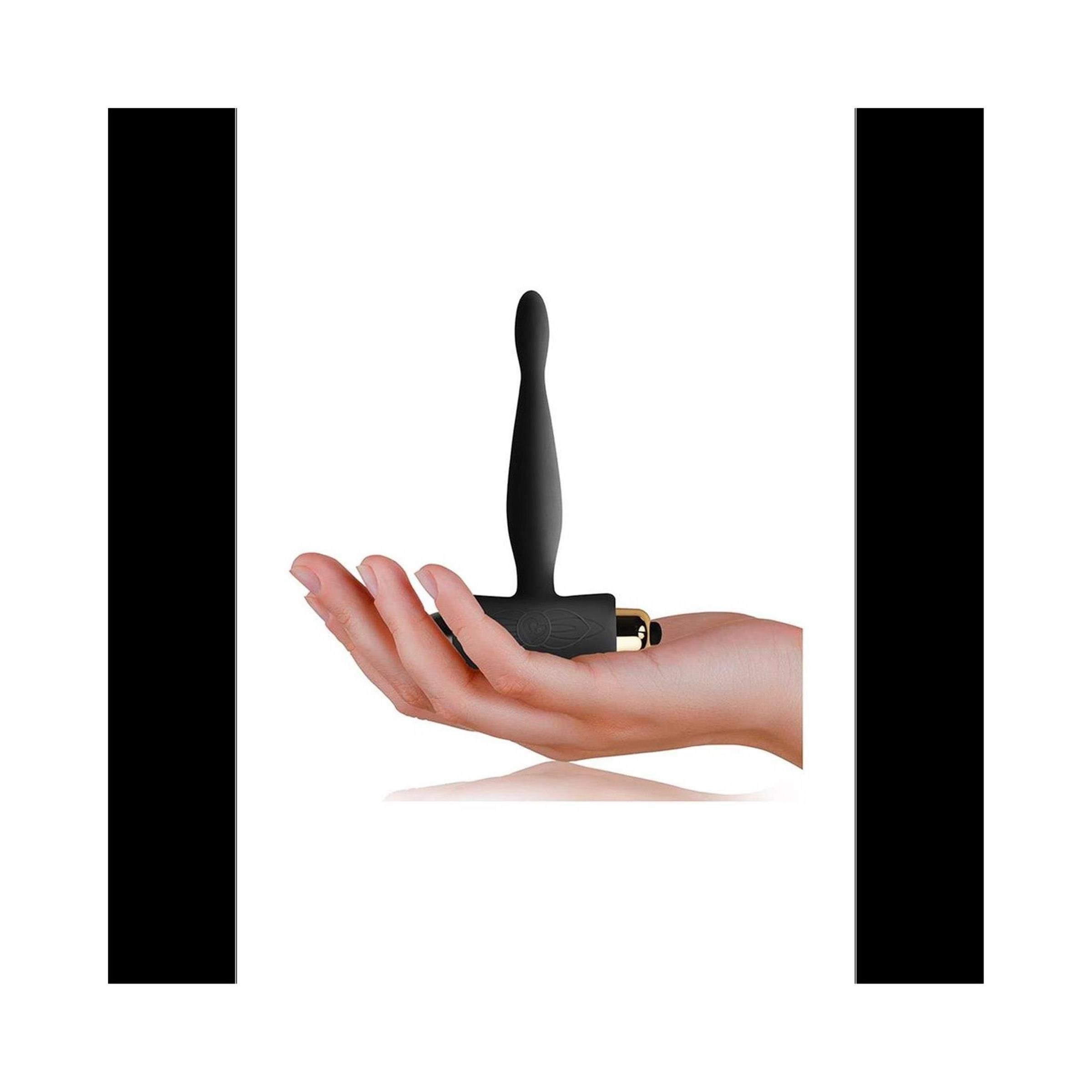 Schwarzes Analspielzeug in einer Hand. Das Produkt hat eine T-Form mit einem Griff und einem abgerundeten Ende.