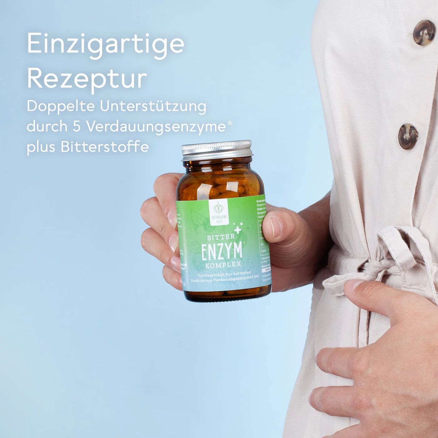 Person hält braune Glasflasche mit grüner Etikett. Aufschrift: BitterLiebe, Bitter Enzym Komplex. Doppelte Unterstützung durch 5 Verdauungsenzyme.