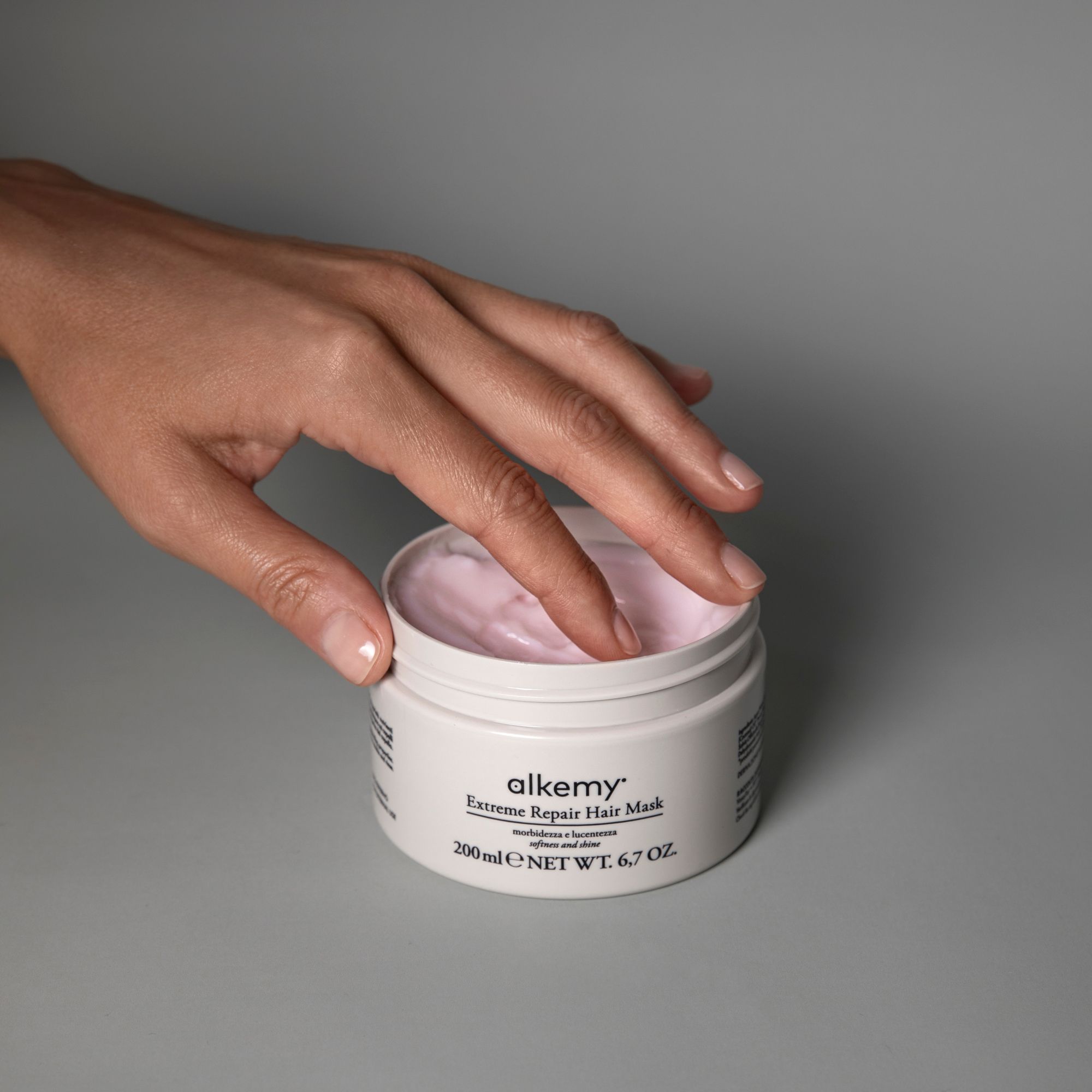 Eine Hand greift in einen offenen Tiegel mit Alkemy Haarmaske.