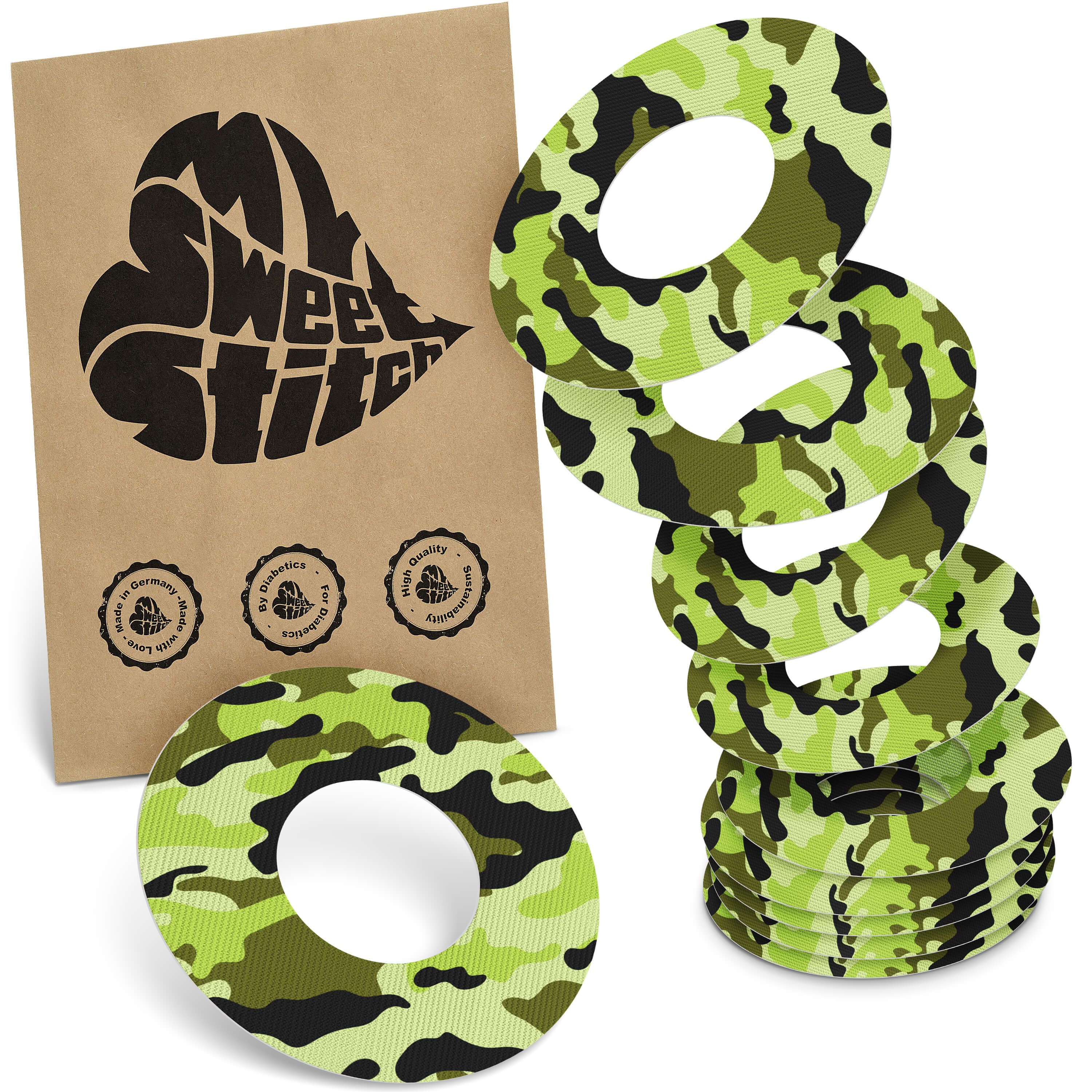 Fixierringe mit Camouflage-Muster. Mehrere Ringe gestapelt und in einer braunen Verpackung mit Logo.