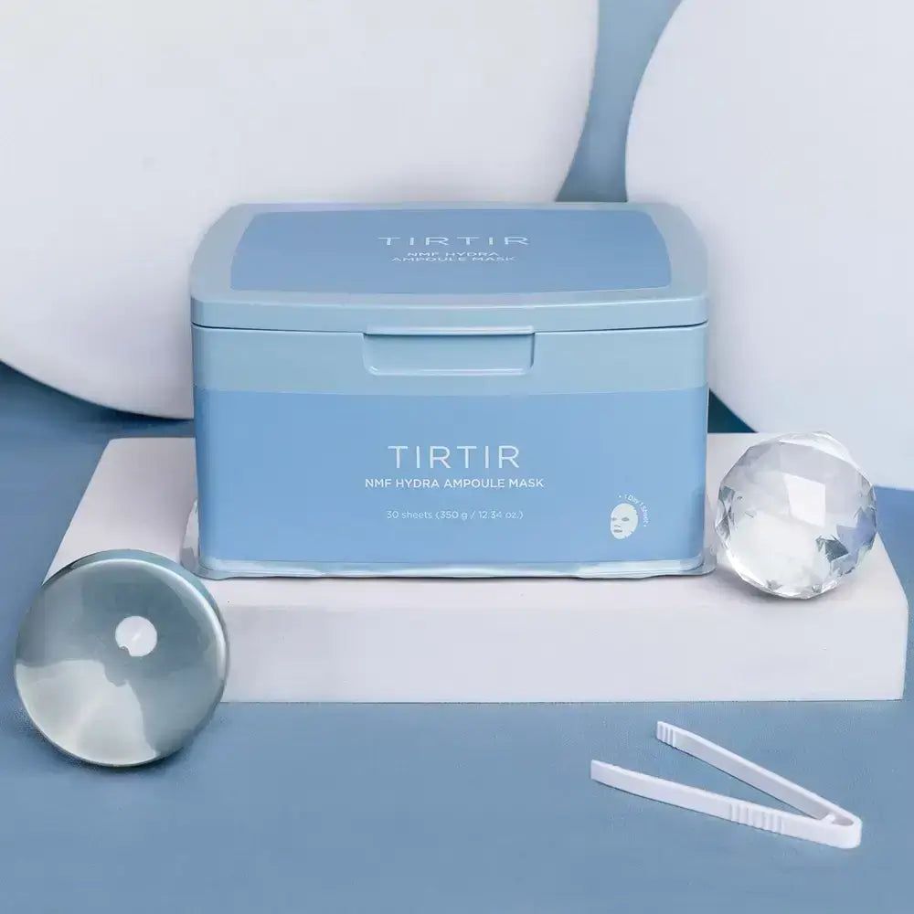 Hellblaue Box mit Deckel. Aufschrift: TIR TIR NMF Hydra Ampoule Mask. Zubehör: Pinzette, runder Behälter, Kristall.