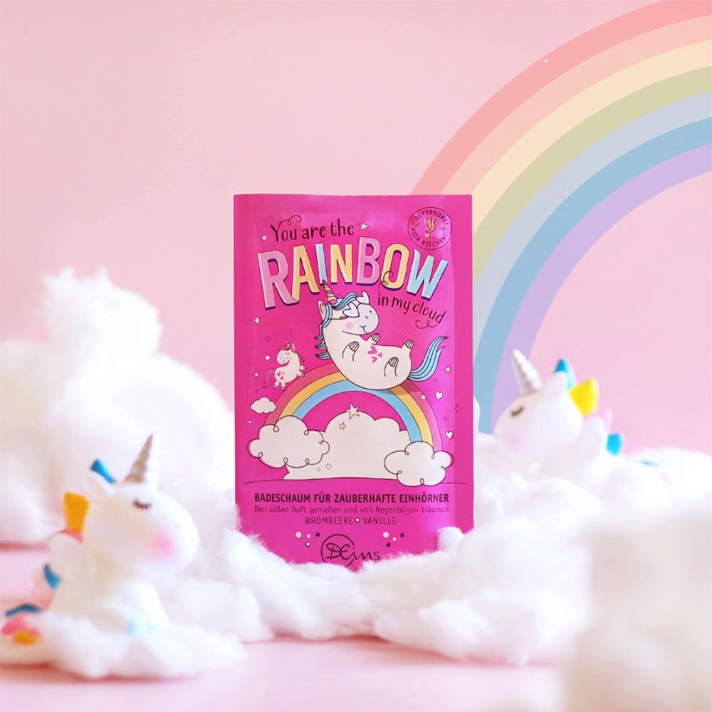 Emballage rose pour bain moussant avec illustration de licorne. Produit entouré de décorations de licorne et de coton. Texte : "You are the rainbow in my cloud".