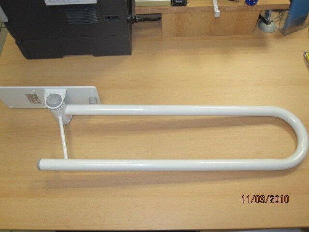 Weißer, klappbarer Haltegriff auf Holzoberfläche. U-Form, mit Wandhalterung. Datum unten rechts.