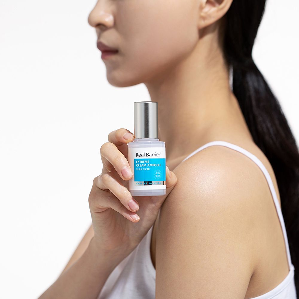 Person hält Serumflasche. Aufschrift: Real Barrier Extreme Cream Ampoule. Silberner Deckel, blaues Etikett.