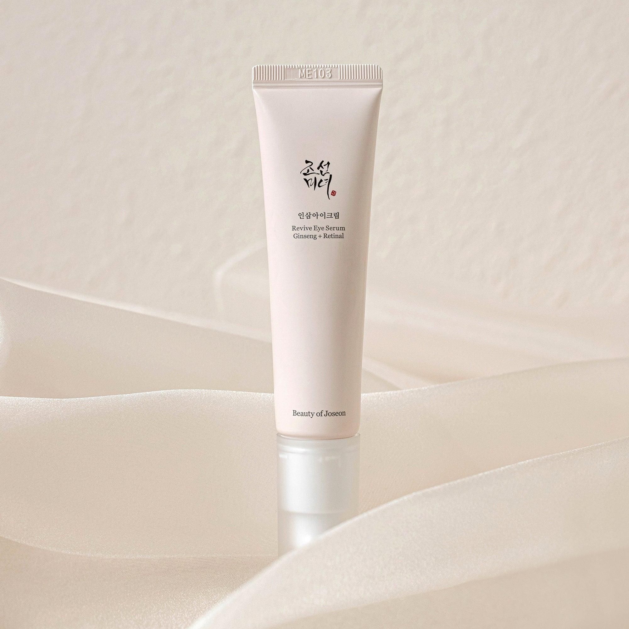 Beige Tube mit weißem Pumpkopf. Auf weißem Stoff. Text: Revive Eye Serum Ginseng + Retinal.