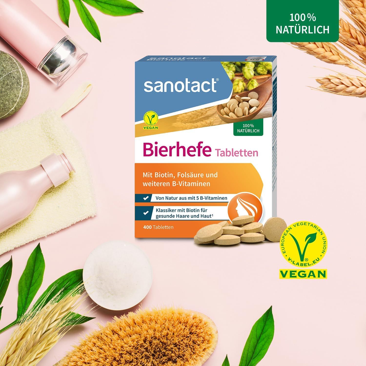 sanotact Bierhefe Tabletten Packung mit Tabletten und Zubehör. Vegan-Siegel. Auf rosa Hintergrund mit dekorativen Elementen.