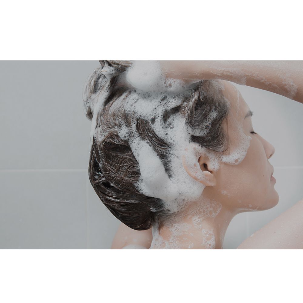 Person wäscht sich die Haare mit Shampoo. Schaum bedeckt das Haar.
