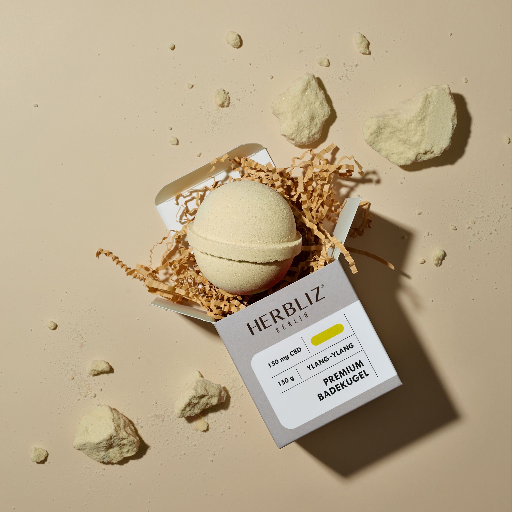 Geöffnete Verpackung mit Badekugel und Dekomaterial. Logo und Produktbezeichnung auf der Verpackung.