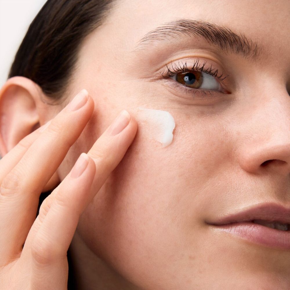 Nahaufnahme einer Frau, die Creme auf ihr Gesicht aufträgt. Helle Haut, Finger berühren die Haut. Creme auf der Wange.