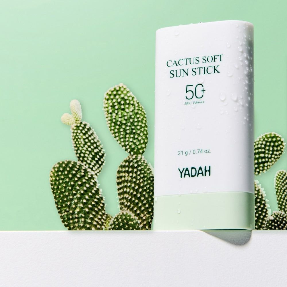 Weiße Sonnencreme-Stiftverpackung mit 'Cactus Soft Sun Stick SPF 50' und 'YADAH' Schriftzug. Daneben Kaktusfeigen.