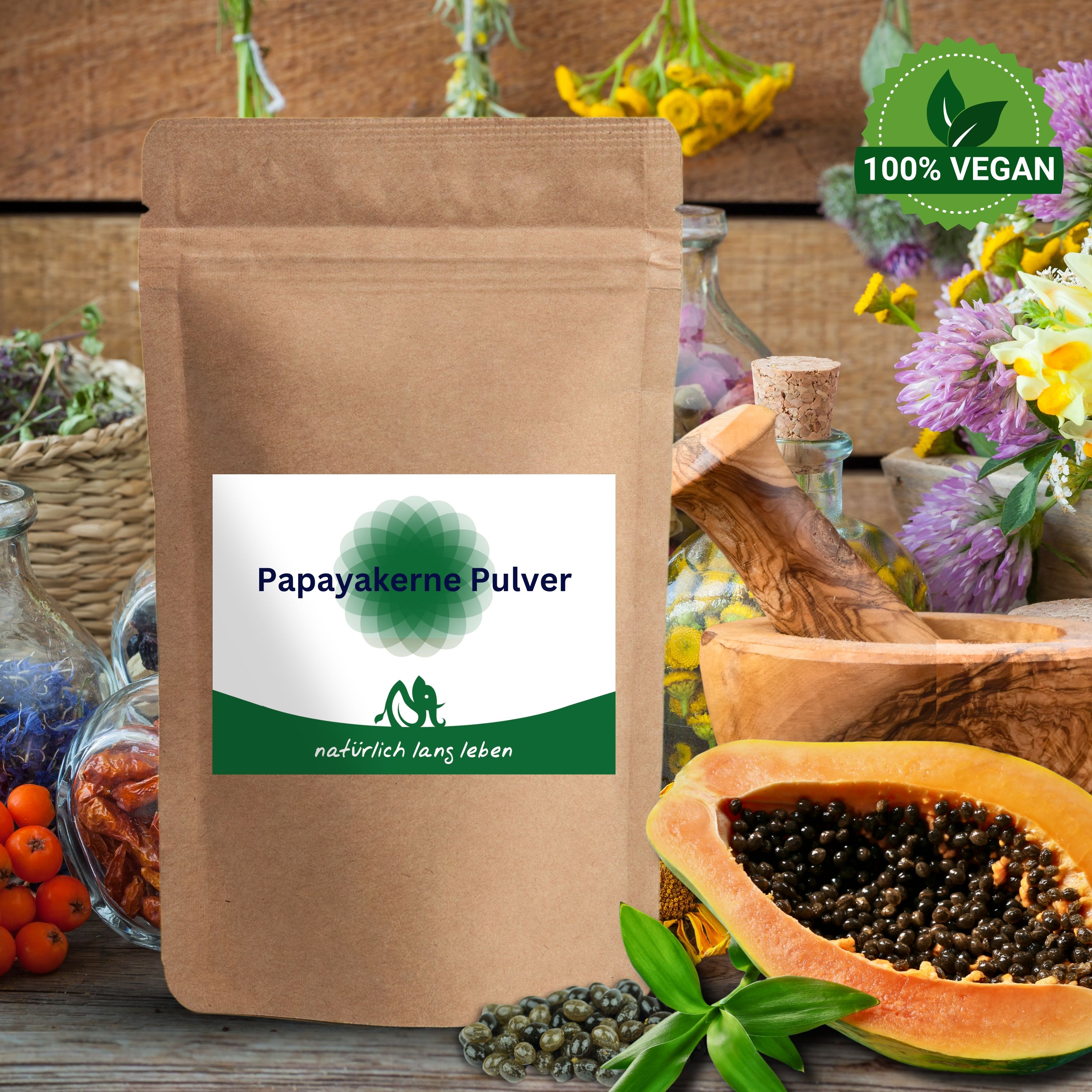 Beutel mit Papayakern-Pulver, neben Papaya-Hälfte, Blättern und Kräutern. Grün-weißes Etikett. Aufschrift: Papayakerne Pulver, natürlich lang leben.