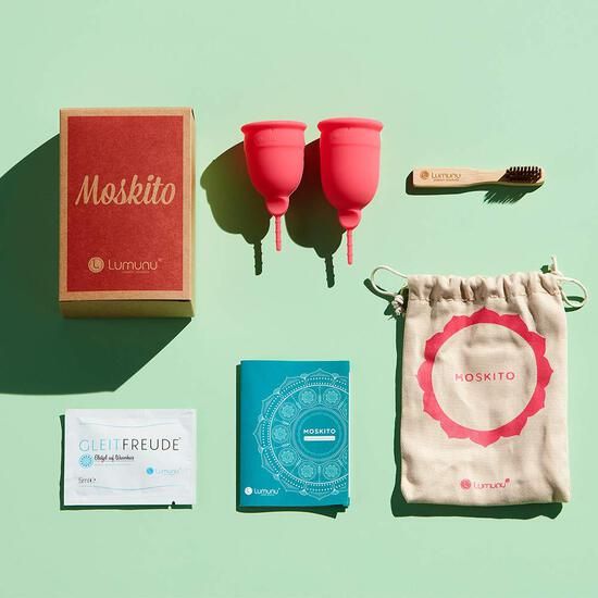 Set mit zwei pinkfarbenen Menstruationstassen, Reinigungsbürste, Beutel, Broschüre und Gleitmittel-Probe.