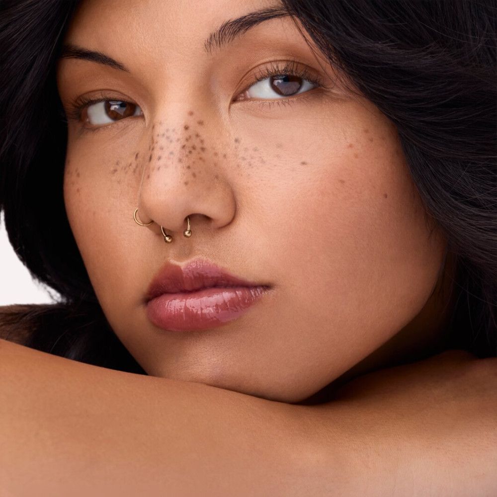 Porträt einer Frau mit Lipgloss auf den Lippen. Dunkle Haare, Sommersprossen. Lippen in einem bräunlichen Farbton.