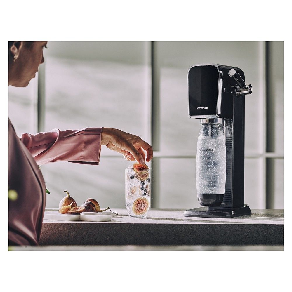 Person gibt Früchte in ein Glas, SodaStream Art im Hintergrund.