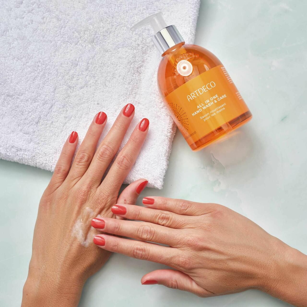 Hände mit rotem Nagellack. Daneben eine Flasche Artdeco All in One Hand Wash & Care und ein weißes Handtuch.