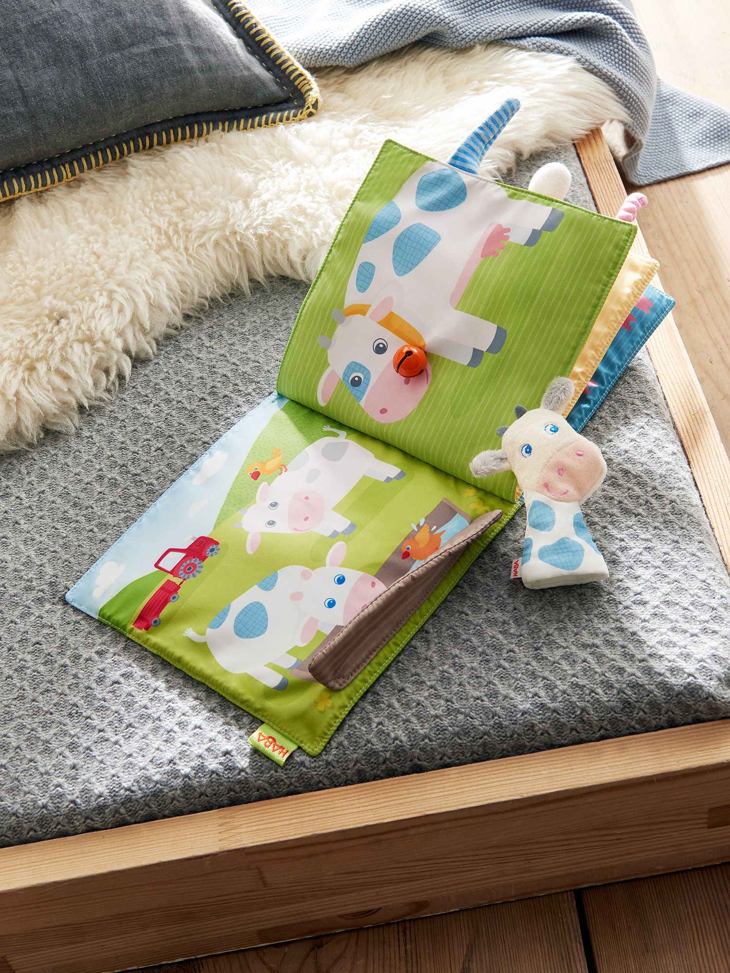 Offenes Stoffbuch Bauernhof. Kühe auf grüner Wiese, Kuh-Fingerpuppe. HABA-Logo unten links.