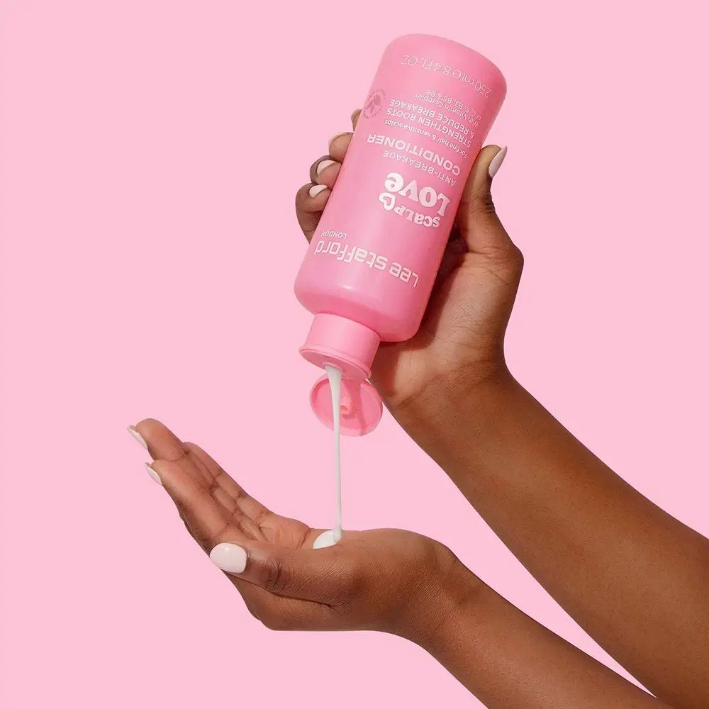 Hände halten eine rosa Flasche LEE STAFFORD Scalp Love Conditioner. Produkt wird in die Hand gegossen. Hintergrund rosa.