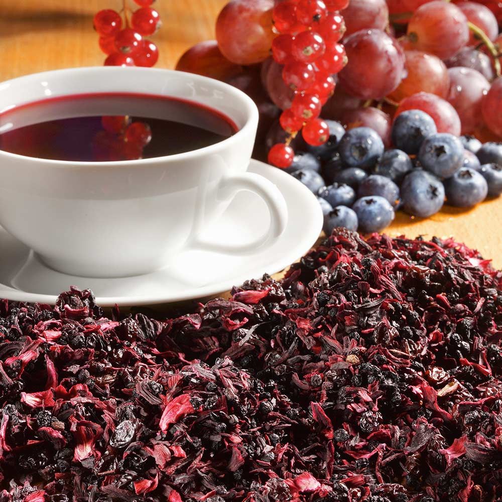 Weißes Tee-Service mit rotem Tee, Trauben und Beeren. Haufen loser Früchtetee auf Holzgrund.