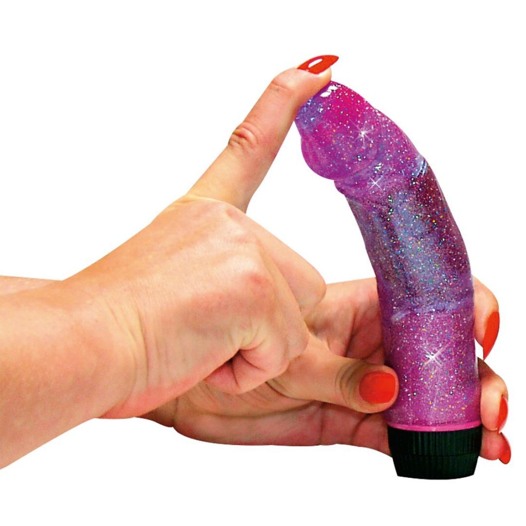 Lila Vibrator mit Glitzer, in Händen gehalten. Zylindrische Form, geriffelte Oberfläche. Schwarzer Sockel.