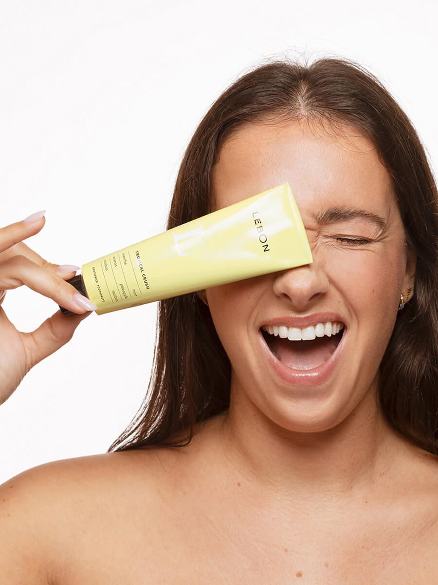 Person hält gelbe Tube vor das Auge. Auf der Tube steht LEBON und Tropical Crush. Die Person lächelt.