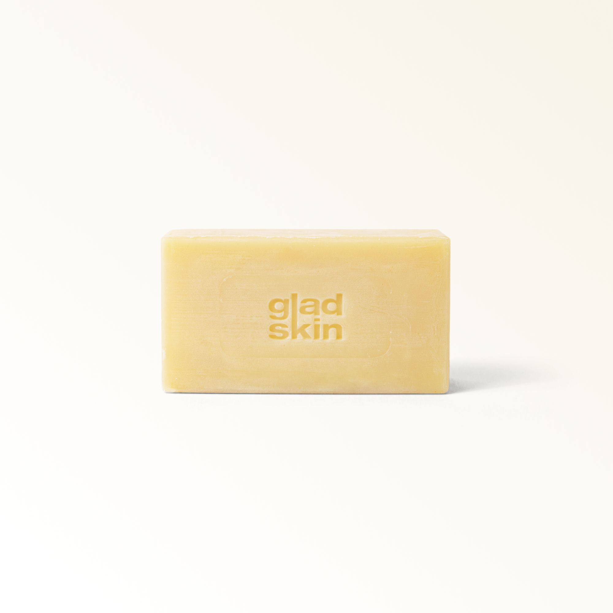 Rechteckiges Seifenstück. Aufschrift: "gladskin". Helles, cremefarbenes Seifenstück auf weißem Hintergrund.