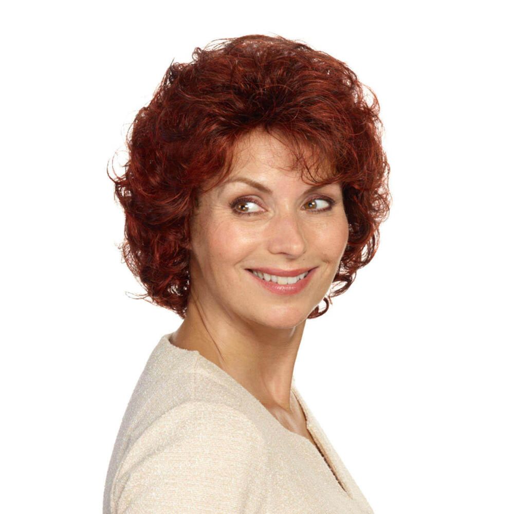 Frau mit roter, lockiger Perücke. Sie trägt ein cremefarbenes Oberteil und lächelt zur Seite.