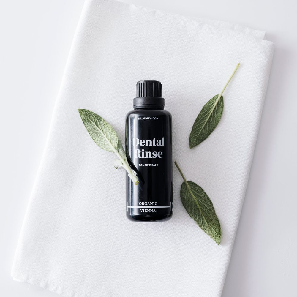 Schwarze Flasche mit schwarzem Deckel, „Dental Rinse“ und „Organic Vienna“ Schriftzug. Auf weißem Tuch mit Blättern.