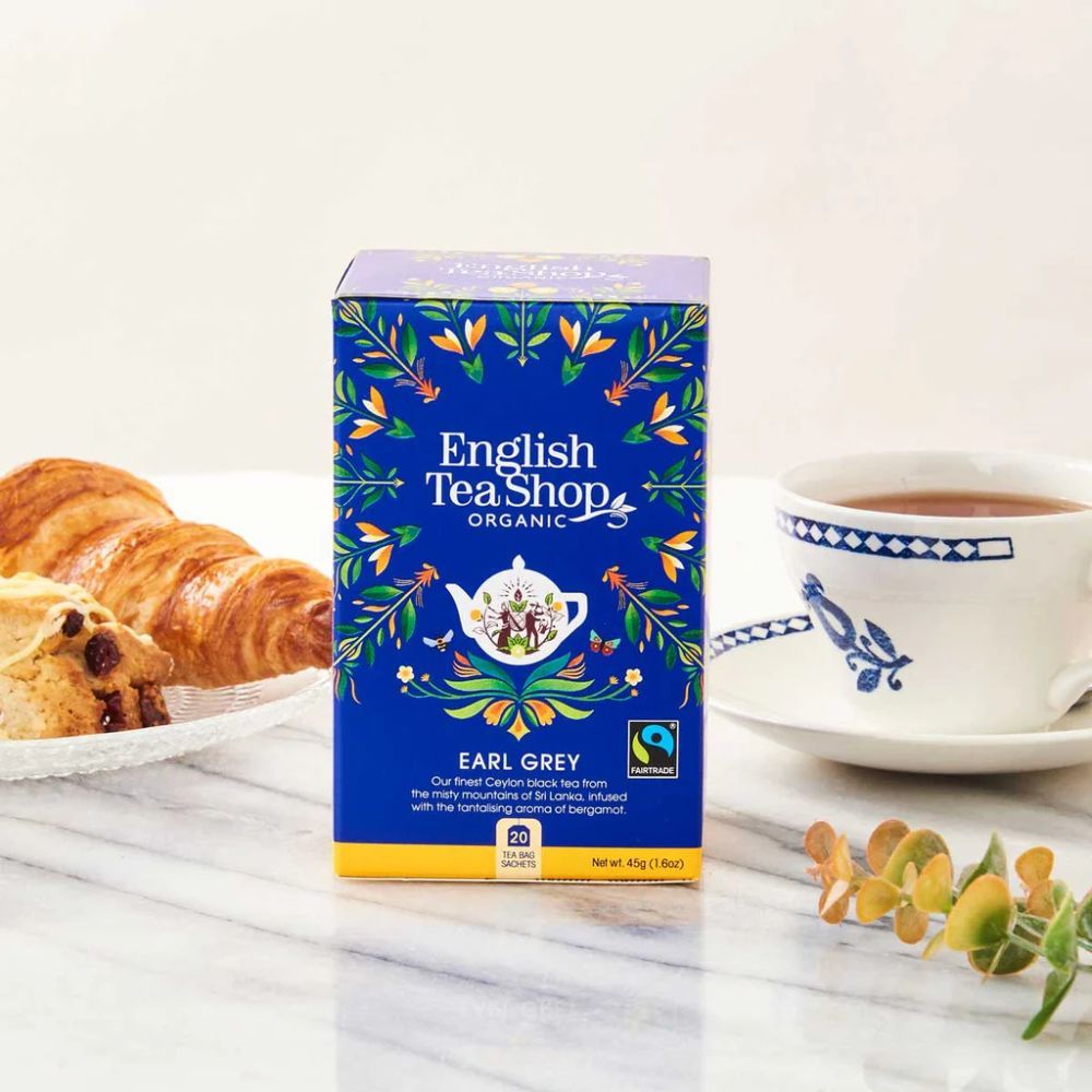Blaue Schachtel mit Aufdruck: English Tea Shop, Earl Grey, Organic. Fairtrade-Siegel. Daneben Gebäck und eine Tasse Tee.
