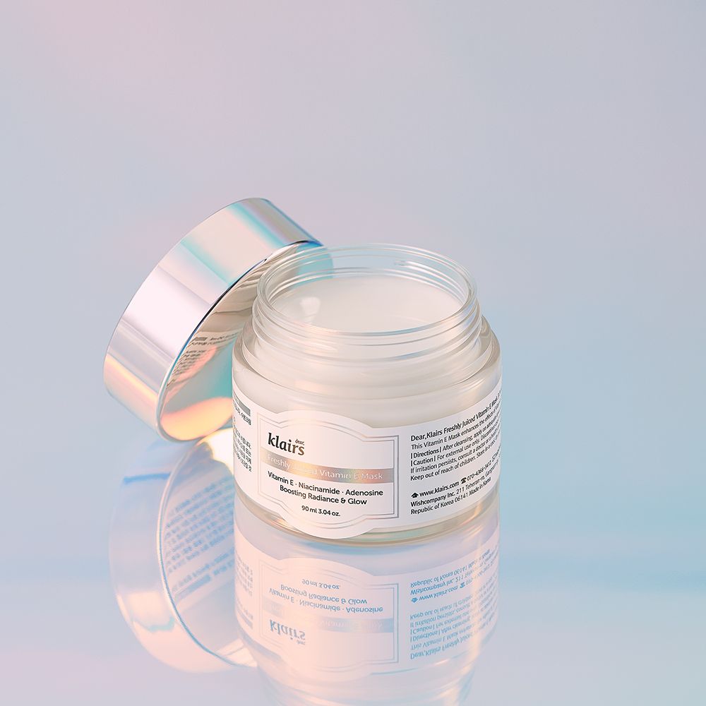 Ein offenes Glas der Freshly Juiced Vitamin E Maske mit silbernem Deckel auf einer reflektierenden Oberfläche.