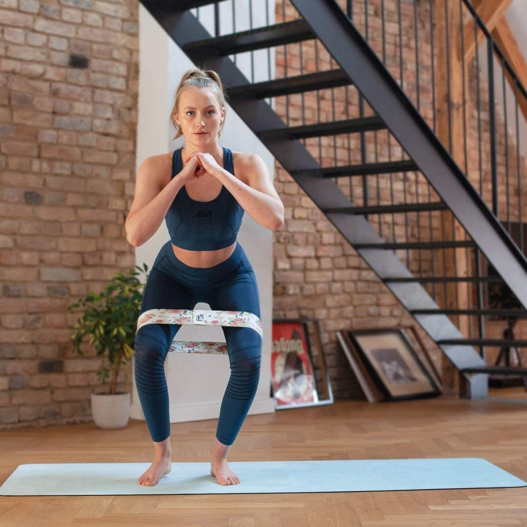 Frau in Sportkleidung beim Squat. Hüftband mit floralem Muster um die Oberschenkel. Auf Yogamatte.
