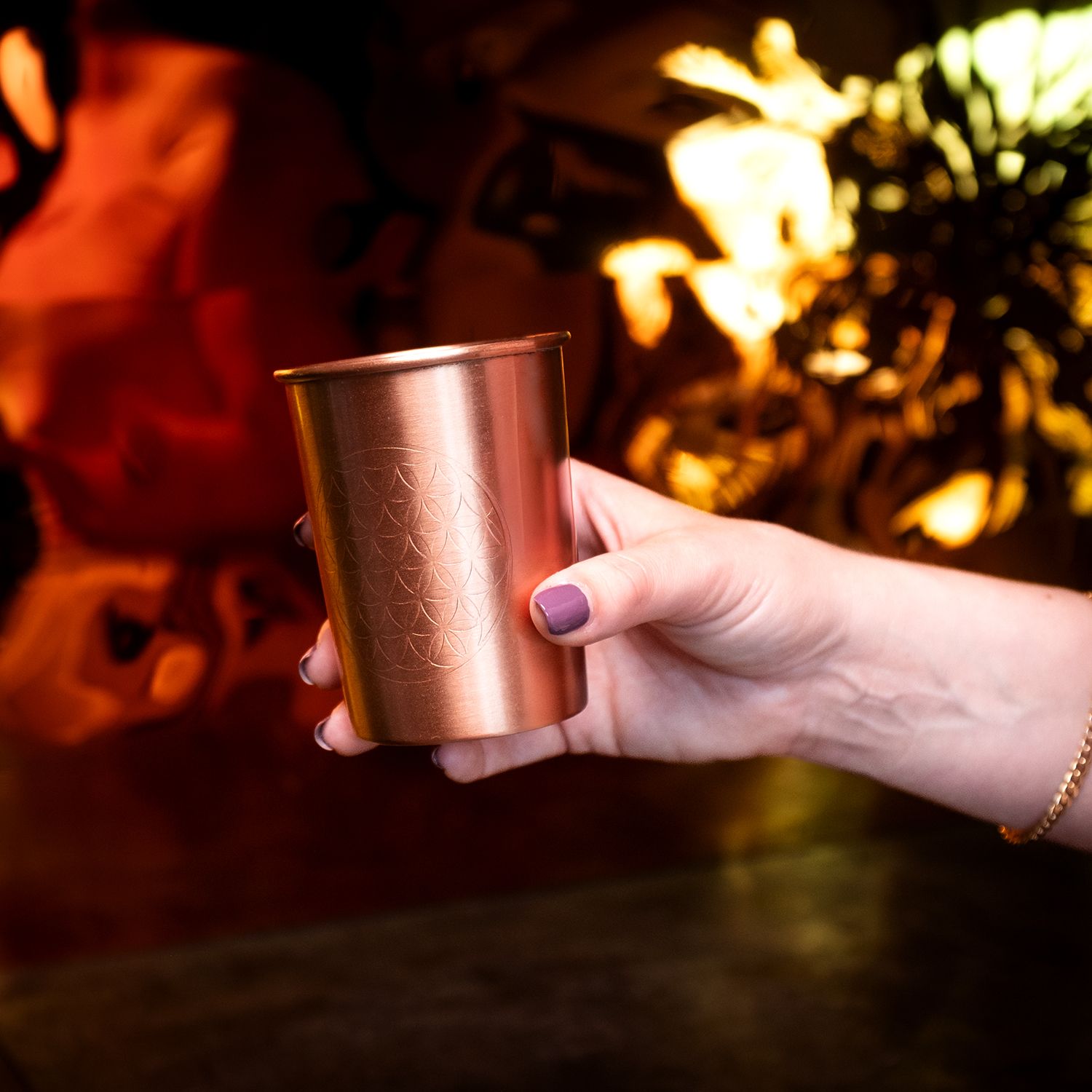 Hand hält Kupferbecher mit Blume des Lebens. Kupferfarbenes Metall, zylindrische Form.