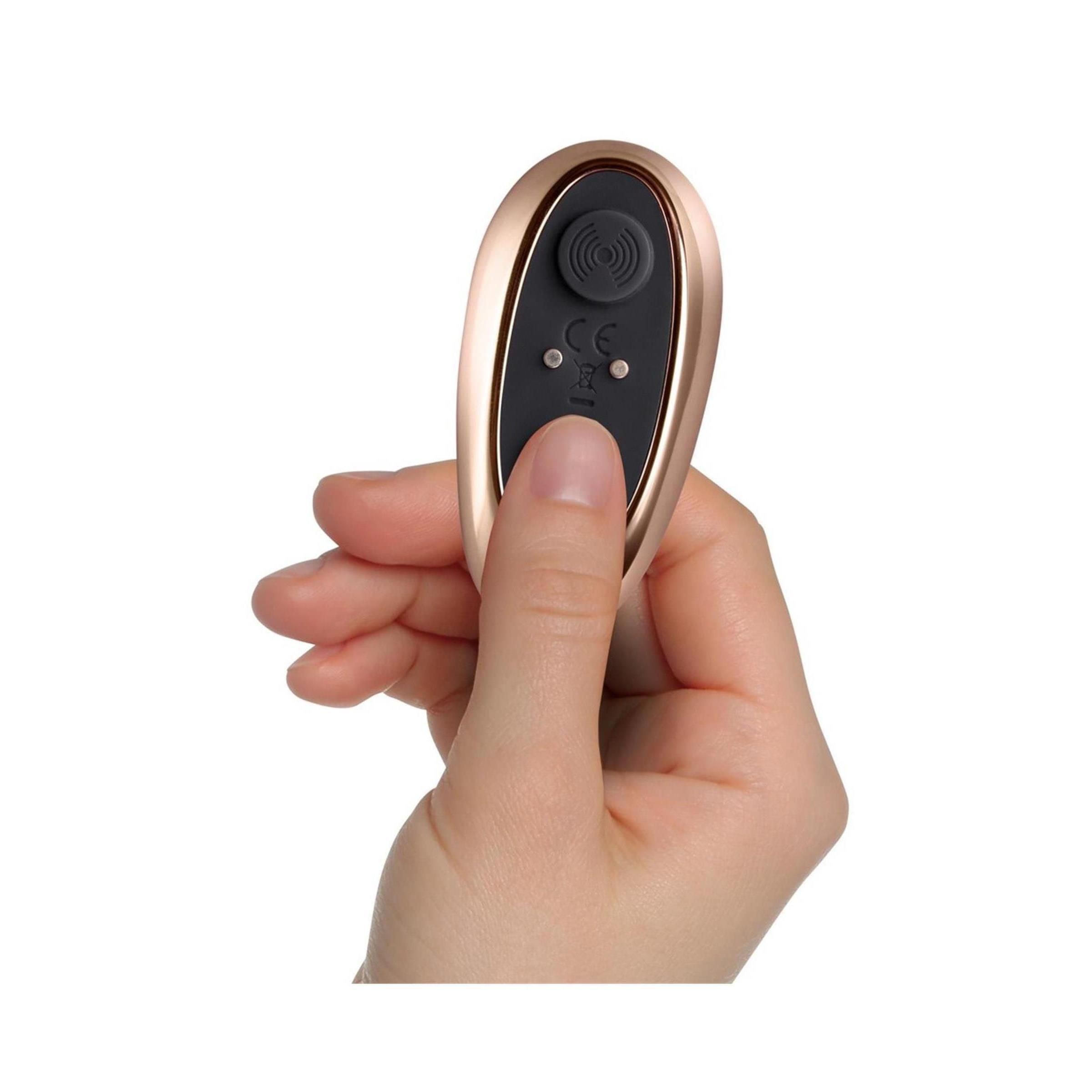 Hand hält goldfarbene Fernbedienung. Schwarze Knöpfe mit Symbolen. CE-Kennzeichnung.