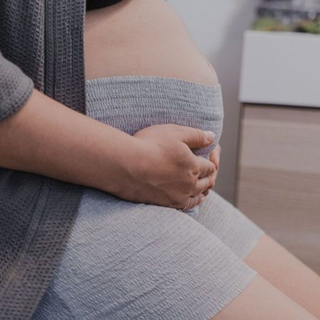Graue Einwegunterwäsche, die von einer Person getragen wird. Die Person sitzt und hält ihren Bauch.