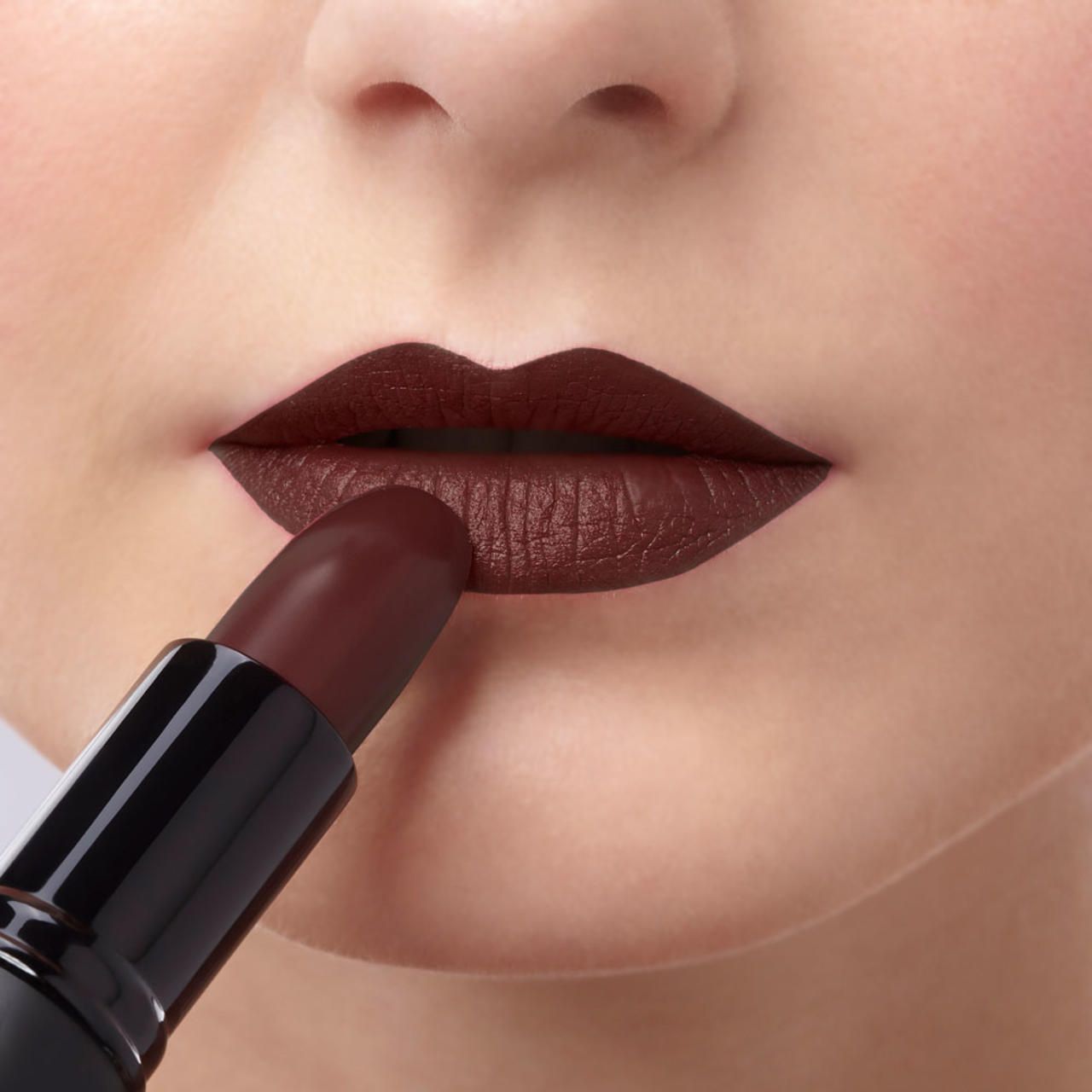 Person trägt burgunderroten Lippenstift auf den Lippen auf. Schwarzer Lippenstift-Stift im Bild.