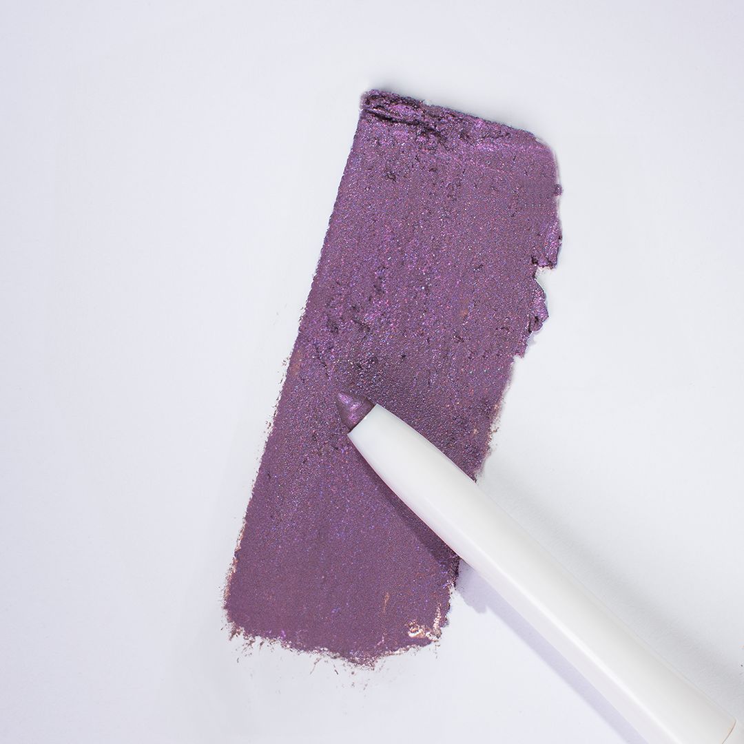Nahaufnahme eines weißen Kajal-Eyeliners, der auf einem Farbmuster in Malve liegt. Der Stift ist teilweise auf dem Farbmuster.