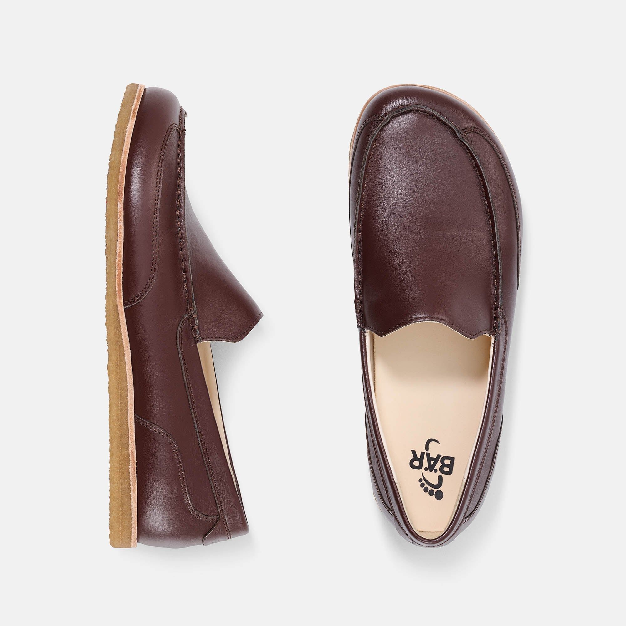 Zwei Slipper. Einer zeigt die Sohle mit Logo. Der andere zeigt die Innenseite mit Logo. Braunes Leder.