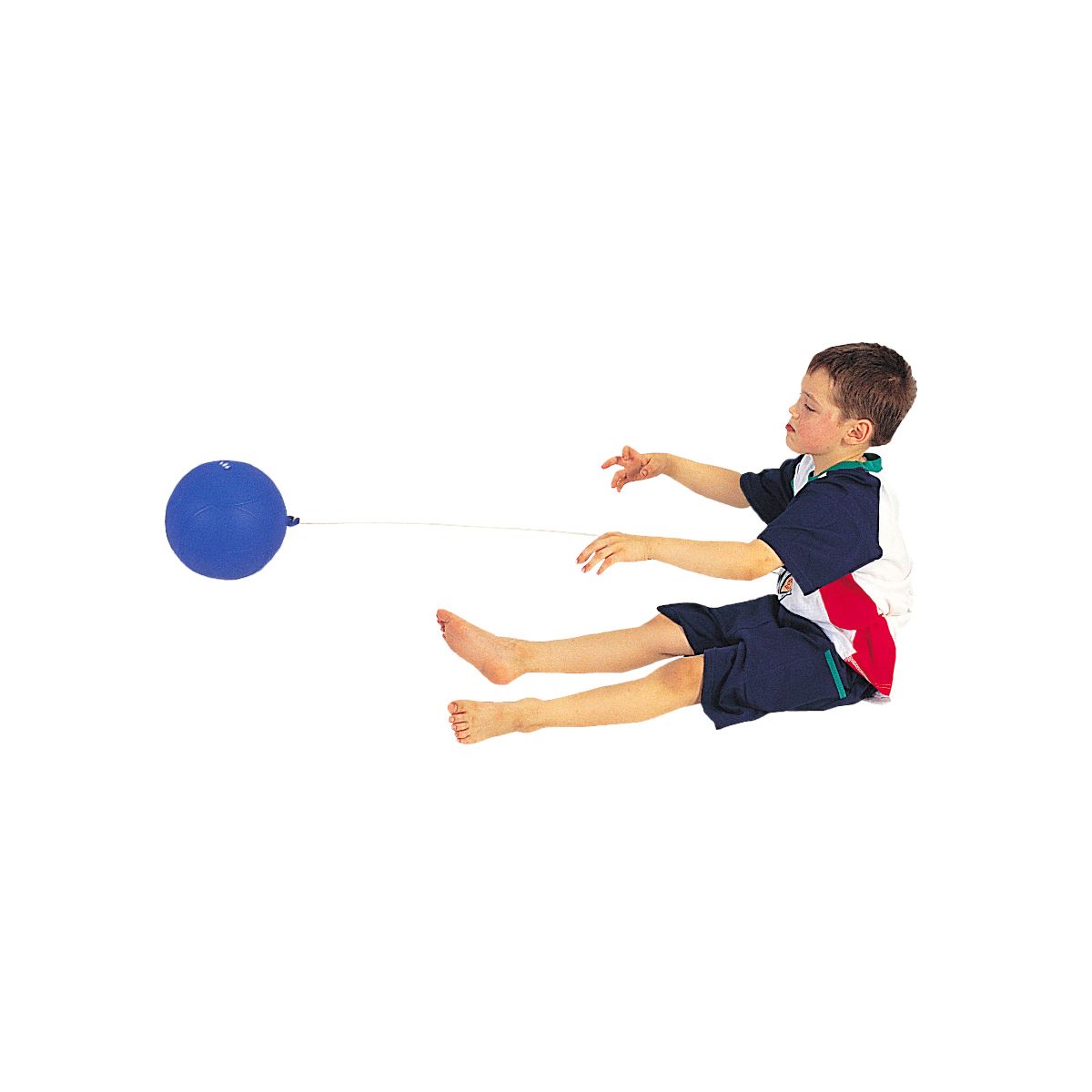 Kind sitzt und greift nach blauem Ball. Ball an Schnur. Kind trägt Shorts.