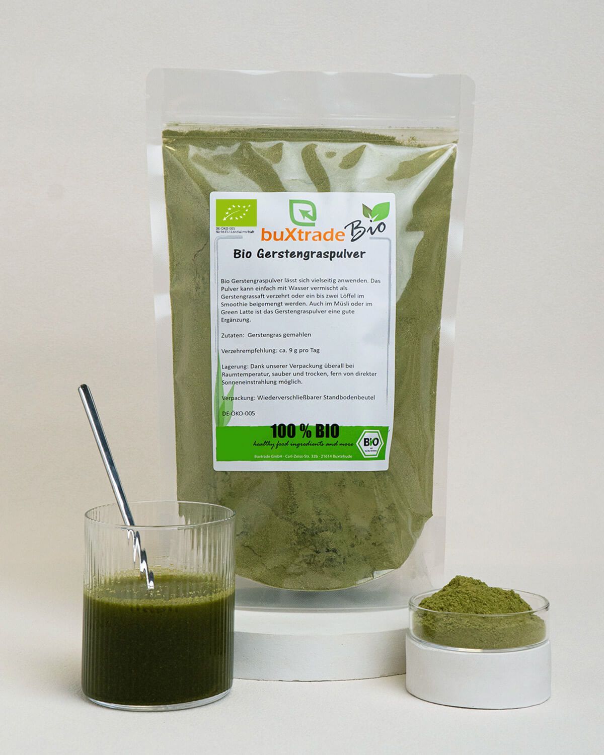 Bio Gerstengraspulver in einem Standbodenbeutel, daneben ein Glas mit grünem Getränk und eine kleine Schale mit Pulver.
