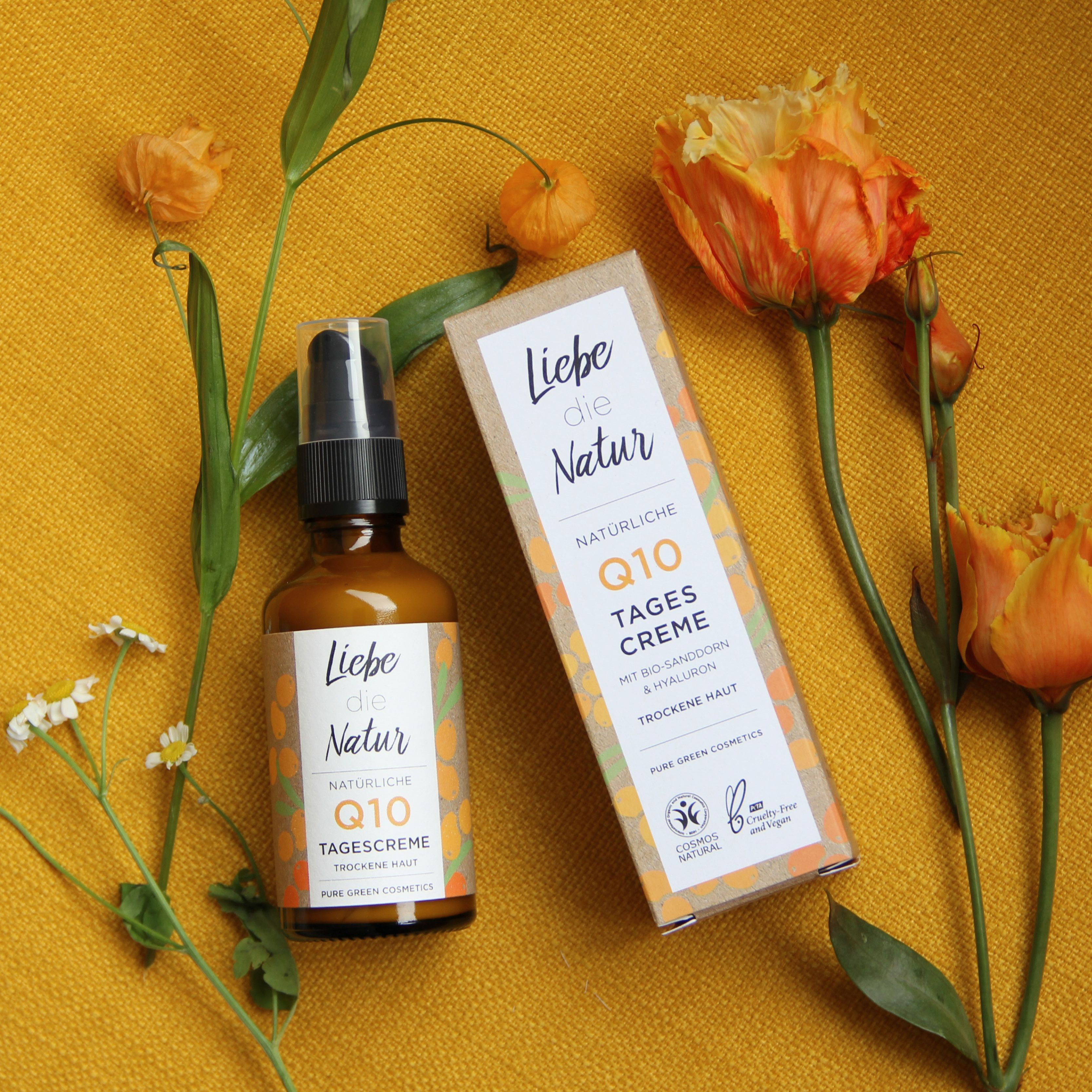 Braune Glasflasche mit Sprühkopf und Karton. Aufschrift: Liebe die Natur, Q10 Tagescreme. Dekoriert mit Blumen auf gelbem Grund.