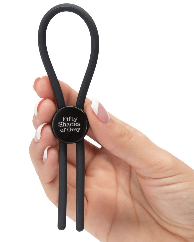Schwarzer Love Ring mit Logo Fifty Shades of Grey, gehalten in einer Hand. Zwei Stränge gehen nach unten.