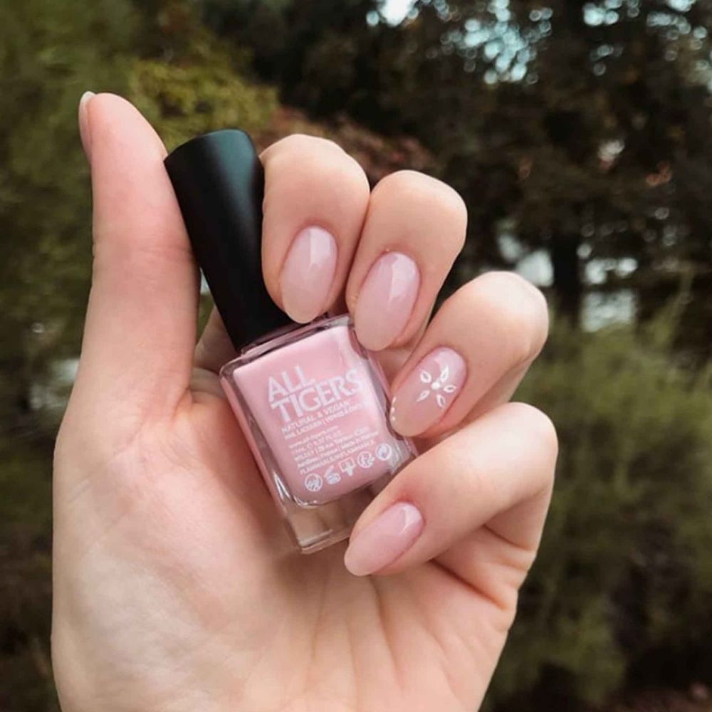Nagellackflasche in Hand gehalten. Aufschrift ALL TIGERS. Lackierte Fingernägel in Rosa.