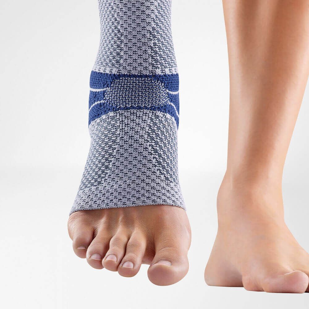 Knöchelbandage am Bein, grau-blaues Strickmuster, anatomische Form. Ohne Fußteil, mit blauen Akzenten und Verstärkungen.