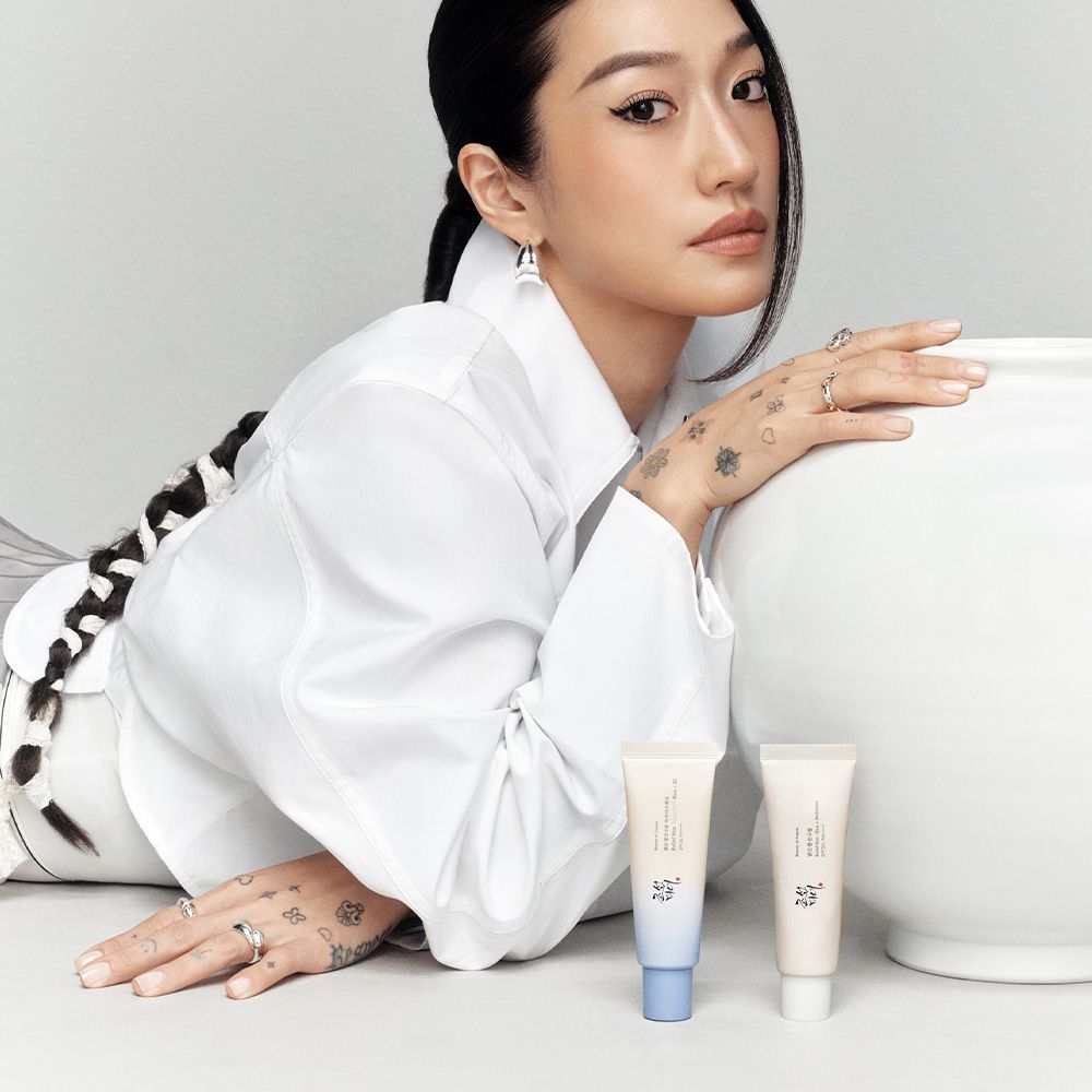 Frau mit zwei Tuben Beauty of Joseon Sonnenschutzcreme neben einer großen Vase.
