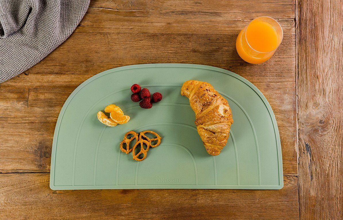 Platzdeckchen mit Croissant, Himbeeren, Mandarinen und Brezeln. Daneben ein Glas Saft.
