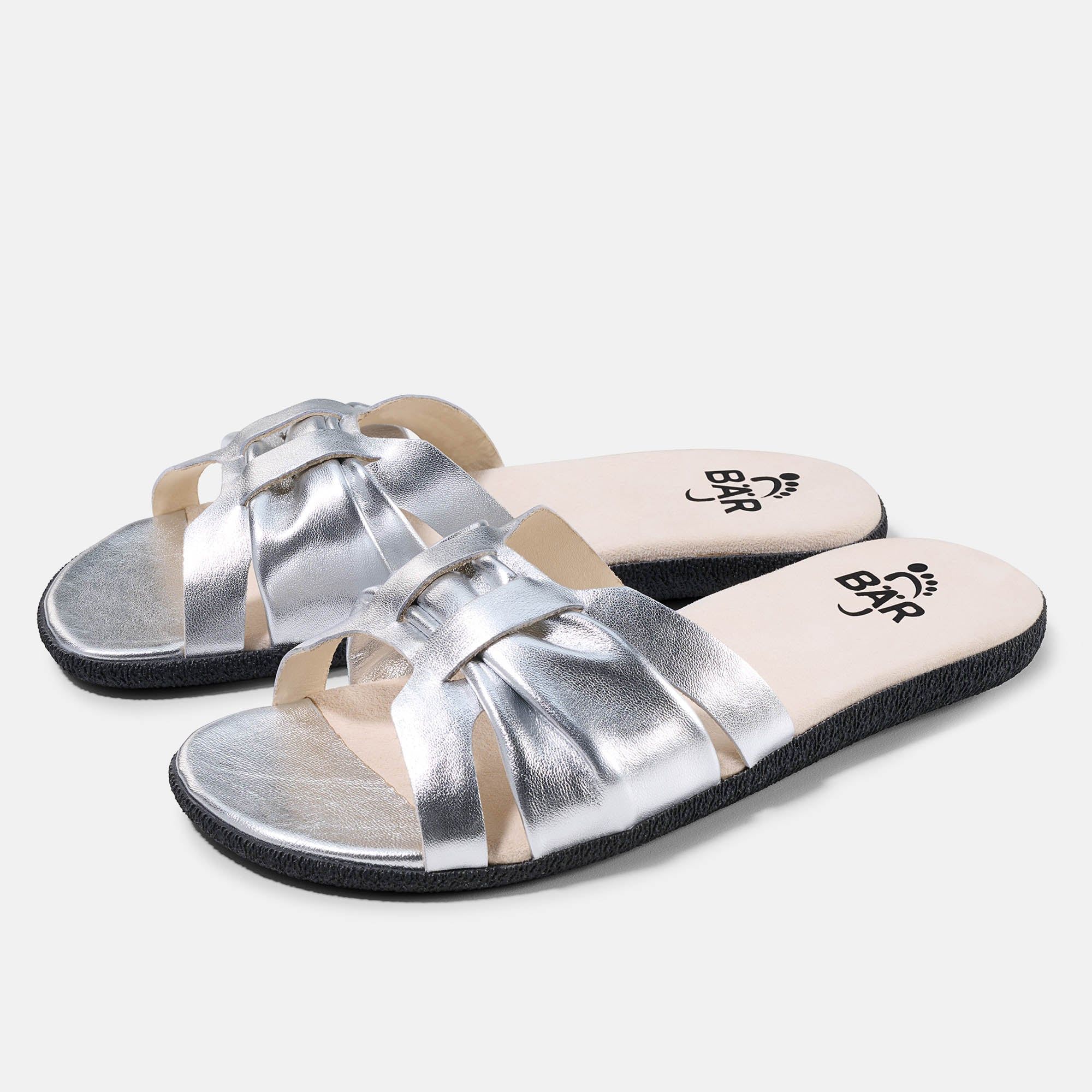 Zwei silberne BÄR Tiana Damen-Pantoletten. Breite Form. Obermaterial mit gekreuzten Riemen. Schwarze Sohle, helle Innensohle mit Logo.