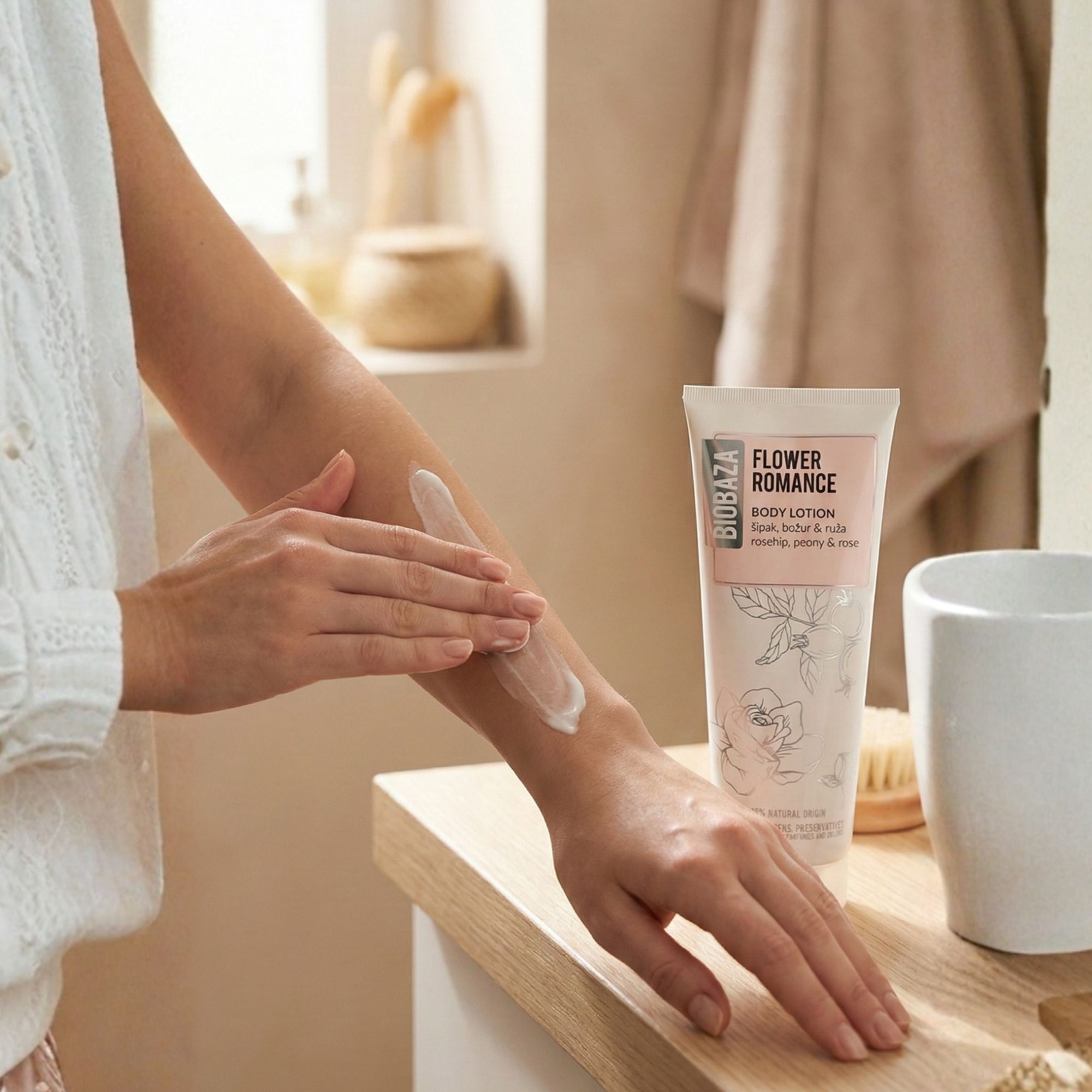 Person trägt Biobaza Body Lotion Flower Romance auf den Arm auf. Badezimmer-Hintergrund mit Waschbecken und Bürste.