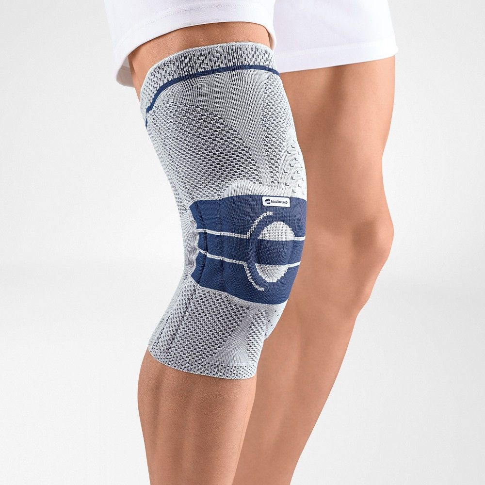 Kniebandage, grau-blau, am Bein getragen. Das Produkt hat eine blaue Verstärkung und das Logo.