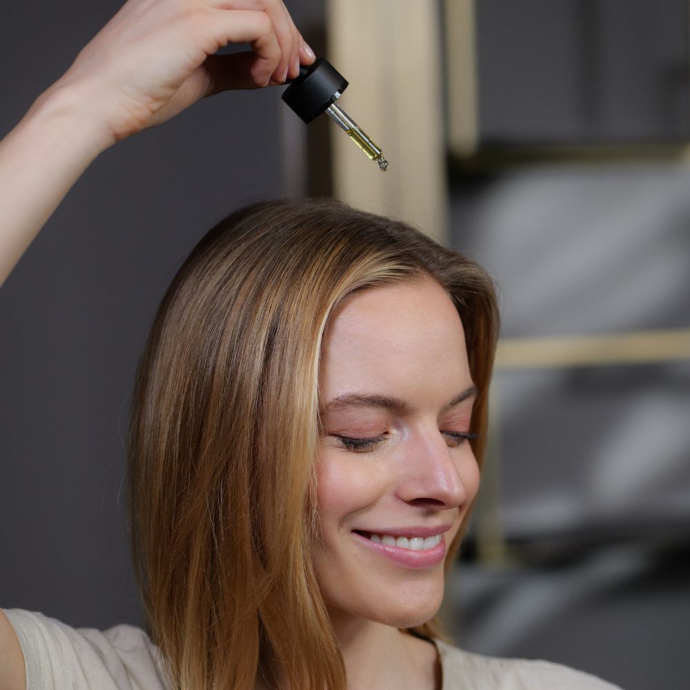 Frau mit Serum-Pipette. Serum wird auf Kopf getropft. Flasche mit schwarzem Deckel.