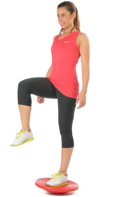 Frau auf rotem Therapiekreisel, Bein angehoben. Sportkleidung.