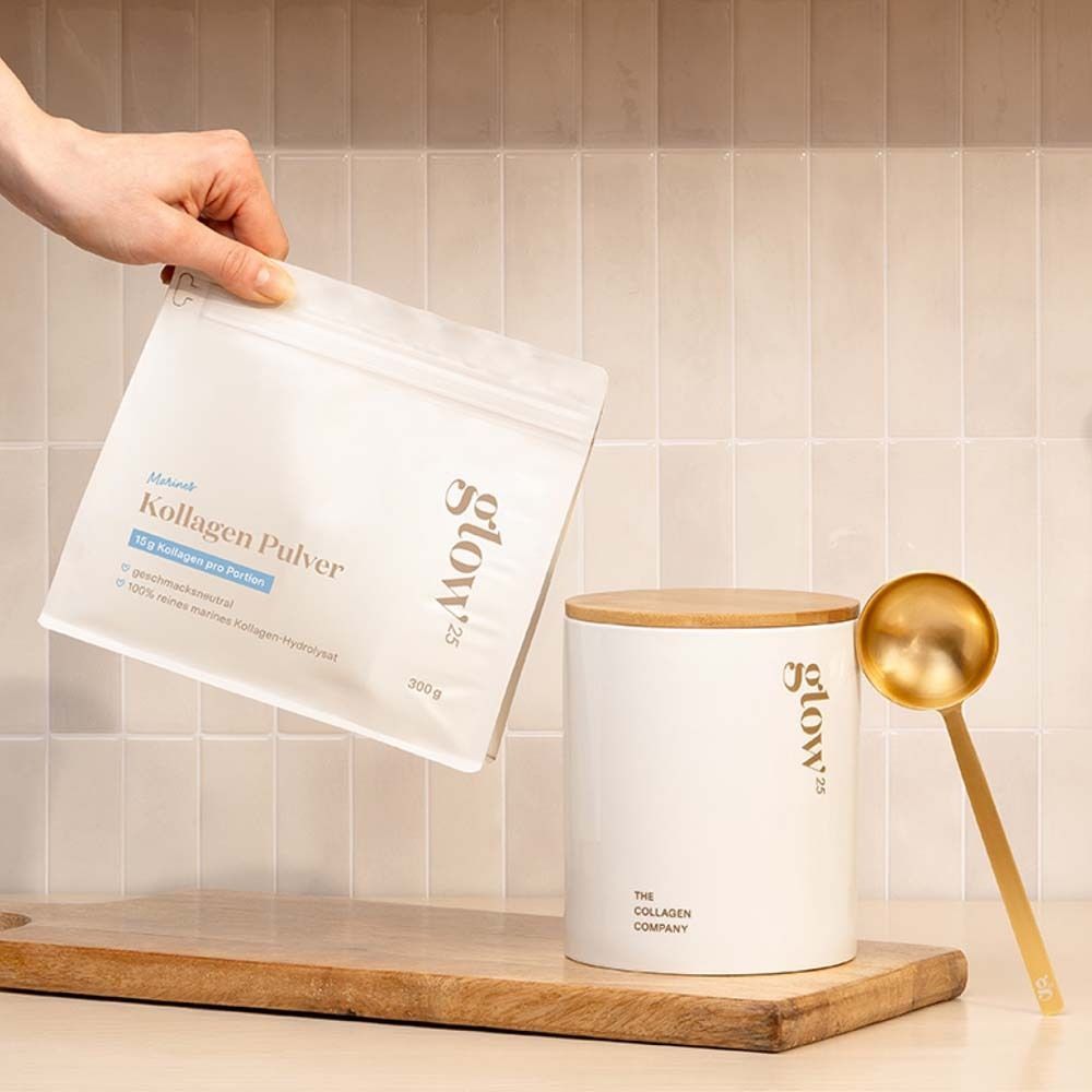 Hand hält eine weiße Tüte mit Kollagenpulver. Daneben ein weißer Behälter mit Holzdeckel und goldener Löffel. Aufschrift: Glow25.
